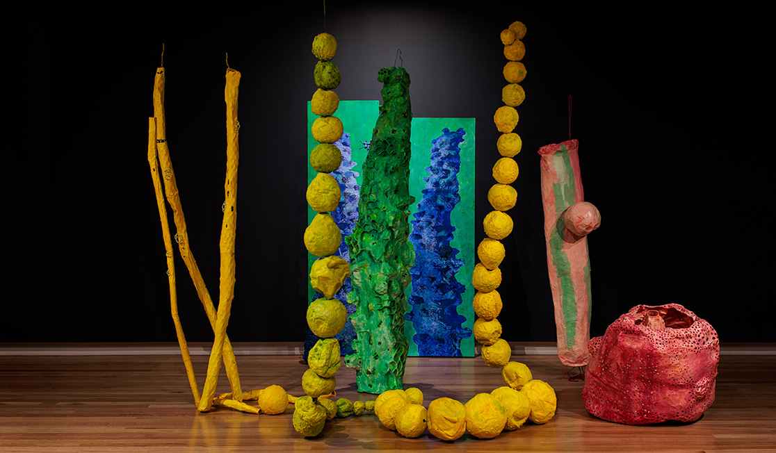 A colourful artwork by Chris DeRosa with brightly coloured papier mache shapes. It is titled Under here my dreams are made of water.